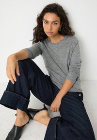 Grå langærmet skjorte med rund hals, parret med mørkeblå brede bukser med opsmøg og sorte slip-on mules.
