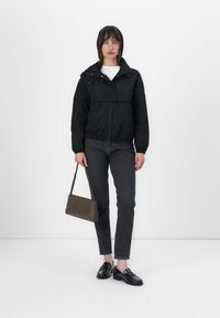 Μαύρη bomber jaket με φερμουάρ μπροστά, ελαστική μέση και δύο κουμπιά σnap, συνδυασμένη με σκούρα τζιν και μια καφέ τσάντα με υφή.