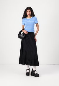 Top a maniche corte blu e gialle a righe con logo "GAP", abbinato a una lunga gonna nera a strati e scarpe con plateau nere. Incluso anche una borsa nera.
