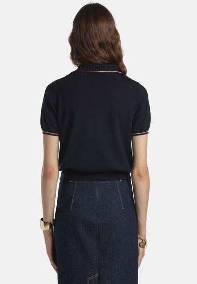 Tricou polo bleumarin tricotat, cu mâneci scurte și guler reiat, prezentând dungi accentuate roșii și albe. Asortat cu o fustă din denim.