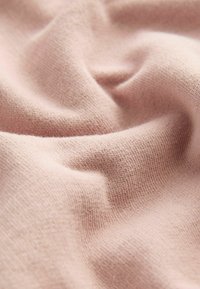 Tissu rose clair avec un tricot doux et texturé. Le matériau semble élastique et lisse, avec des variations subtiles d'épaisseur.