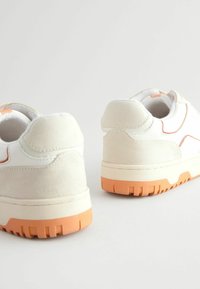 Sneakers z białej, gładkiej skóry oraz jasnoszarego zamszu, z pomarańczowymi akcentami i teksturowaną gumową podeszwą. O zaokrąglonym kształcie z wyściełanym kołnierzem.