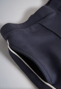 Gros plan d'un vêtement en tissu gris foncé avec un bord blanc et un détail plié sur un fond clair.