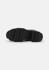 Semelle de chaussure en caoutchouc noir présentant une texture striée, des bords arrondis et une forme effilée, conçue pour l'adhérence et la durabilité.
