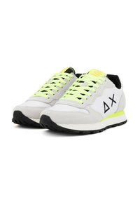 Une paire de baskets blanches et grises avec des lacets jaunes néon, des semelles noires et un logo noir sur le côté, positionnées côte à côte.