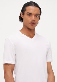 Weißes Kurzarm-V-Ausschnitt-T-Shirt aus einem glatten Baumwollmix, das ein figurschmeichelndes Design und subtile Nähdetails aufweist.