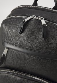Black textured leather backpack featuring silver zippers, a front pocket, and a subtle embossed logo for detail. Smooth accents enhance design.