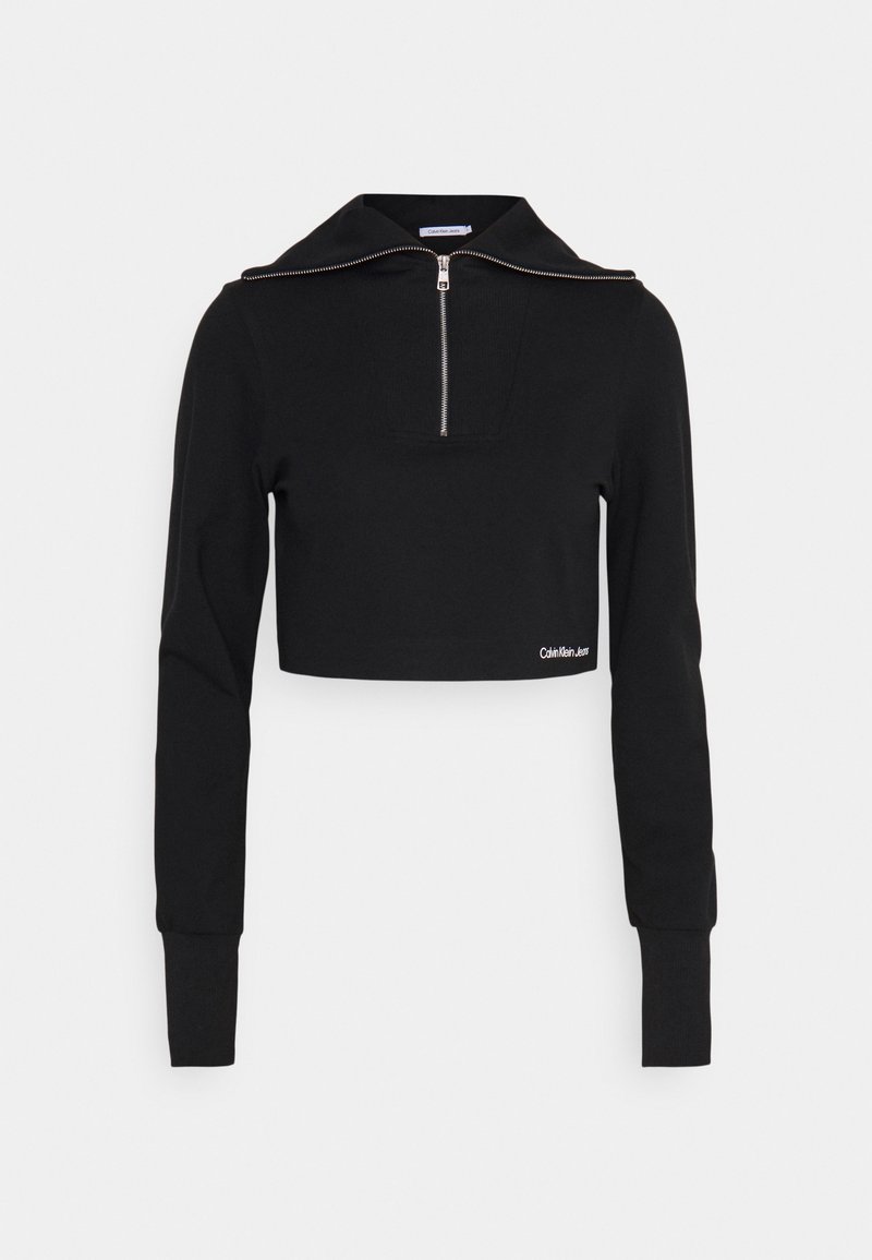 Svart kort sweatshirt med dragkedja vid kragen, ribbad textur och långa ärmar. Har en liten vit logotyp vid fållen.