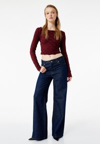 Bordeaux langetermijn mouw cropped top met textuurpatroon, gecombineerd met high-waisted donkerblauwe wijde jeans en zwarte puntige hakschoenen.