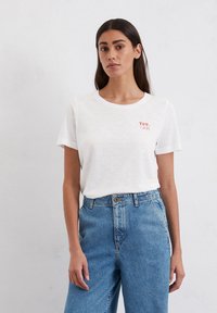 White short-sleeve t-shirt with a round neckline, featuring a red printed text "You. Me." on the left chest. Paired with high-waisted blue jeans.
