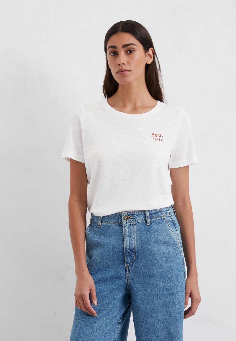 White short-sleeve t-shirt with a round neckline, featuring a red printed text "You. Me." on the left chest. Paired with high-waisted blue jeans.