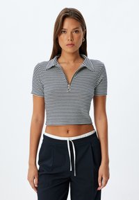 Randig crop-top i svart och vitt med dragkedjekrage och korta ärmar, tillverkad av ett lätt, texturerat material.