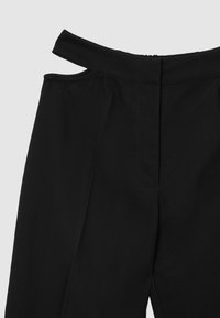 Pantalons noirs ajustés avec une taille haute, des découpes sur les côtés et un tissu lisse et texturé. Fermeture éclair à l'arrière.