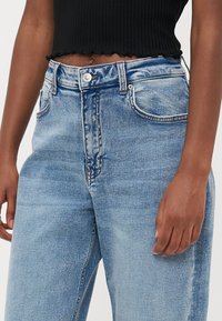 Ανοιχτό μπλε τζιν παντελόνι με ψηλή μέση και χαλαρή εφαρμογή, διαθέτοντας κλείσιμο με κουμπί, πέντε τσέπες και λεπτομέρειες ελαφριάς ξεθωριασμένης όψης.