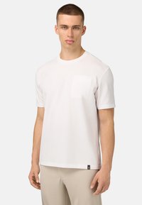 T-shirt bianco in cotone a maniche corte, con una piccola tasca sul petto e un discreto etichetta del marchio sull'orlo. Texture liscia e vestibilità rilassata.
