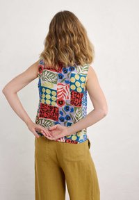 Bezrokavni top z obarvano patchwork zasnovo, ki vključuje cvetlične in geometrijske vzorce v rdeči, modri, zeleni in rumeni barvi na svetlem ozadju.