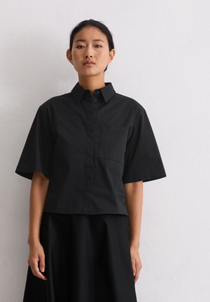 Chemise noire à manches courtes avec un col et une poche poitrine unique. Fabriquée en tissu lisse, avec un design cropped.