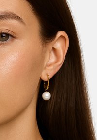 Gullringene har en enkel hvit perle vedhengt. Ringen er glatt, mens perlen har en blank overflate.