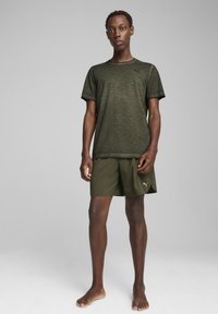 Camiseta deportiva de color verde oliva con un patrón texturizado, combinada con pantalones cortos a juego que presentan el logo de Puma. Diseño ligero y de manga corta.