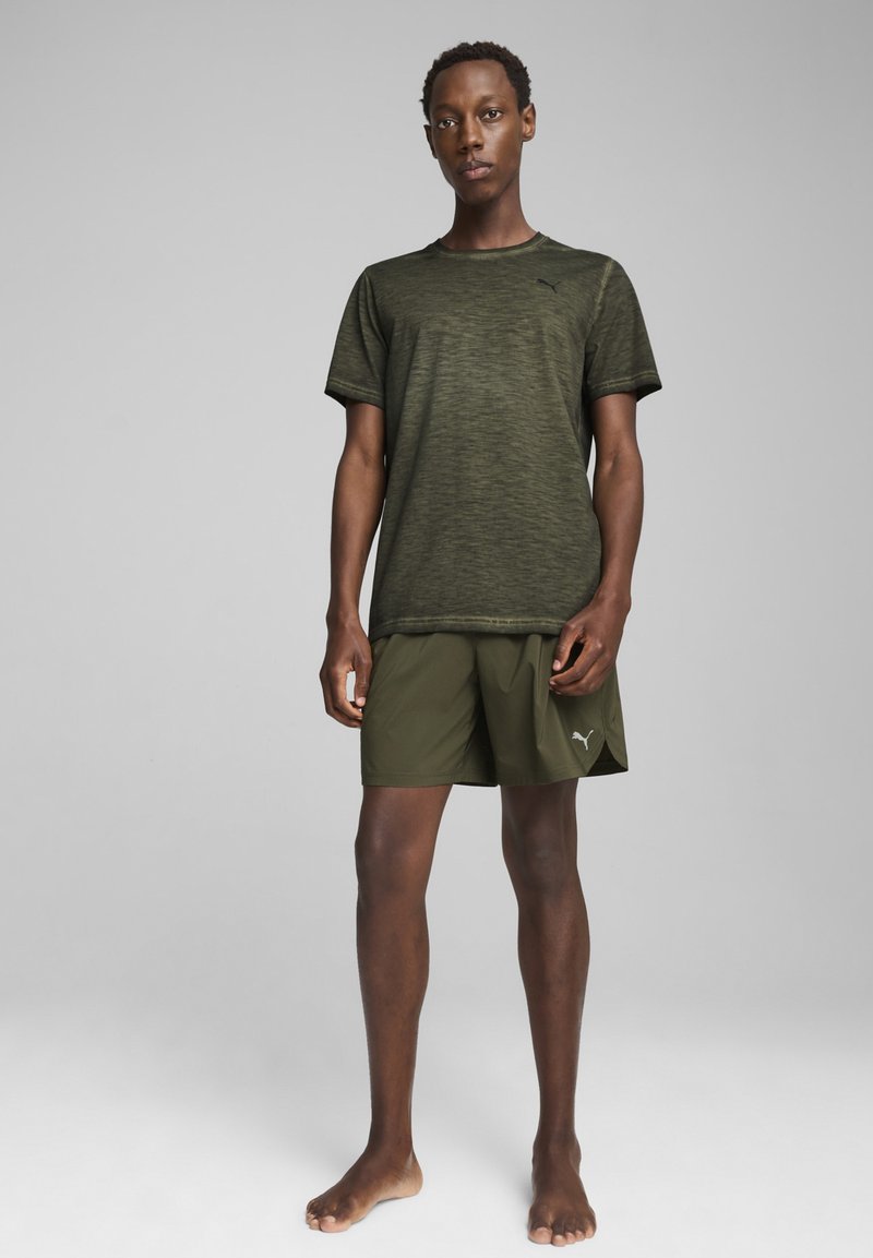 Camiseta deportiva de color verde oliva con un patrón texturizado, combinada con pantalones cortos a juego que presentan el logo de Puma. Diseño ligero y de manga corta.