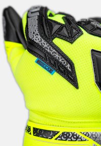 Hochsichtbare gelbe Handschuhe mit strukturierten schwarzen Akzenten, hexagonalem Muster und verstärkten Teilen. Mit einem blauen Etikett und Details am Handgelenk.