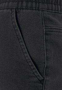 Schwarze Jeans mit seitlicher Tasche, flachen Nähten und glatter Textur. Der Bund ist elastisch für zusätzlichen Komfort.