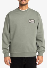 Lichtgroene sweatshirt met lange mouwen, geribde manchetten en een ronde halslijn. Bevat een geborduurd patch met een cobra ontwerp.