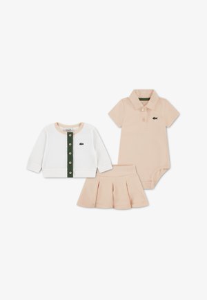 Ensemble de vêtements pour enfants en trois pièces : cardigan blanc côtelé avec boutons verts, body polo pêche, et jupe plissée pêche. Comprend le logo Lacoste.