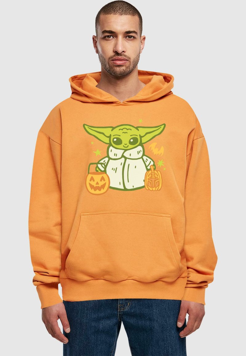 Oranžová mikina má velký grafický motiv postavy se zelenou pokožkou, která drží dvě dýně na Halloween. Má přední kapsu a kapuci.