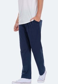 Marineblaue, locker sitzende Hose aus weichem Stoff, mit seitlichen Taschen und elastischem Bund, getragen mit einem weißen T-Shirt und weißen Sneakers.