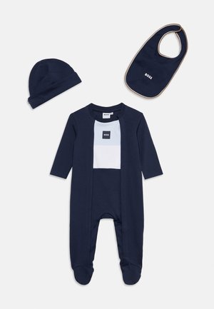 Ensemble bébé bleu marine avec grenouillère à pieds, bonnet assorti et bavoir, tous portant le nom de la marque BOSS en blanc.