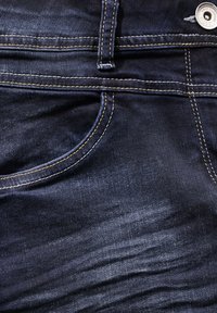 Donkerblauwe denim jeans met een klassieke pasvorm, voorzien van een voorkeuzezak, oranje stiksels en een zilveren metalen knoop in de taille.