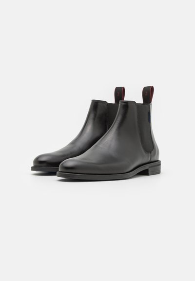 Black leather Chelsea boots with elastic side panels, flat heel, and red accent pull tabs on the back. Smooth finish with minimal stitching.