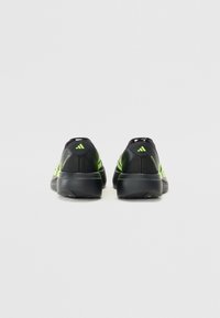 Schwarze Sportschuhe mit grünen Akzenten, ausgestattet mit einem strukturierten Obermaterial, einer gepolsterten Sohle und einem auffälligen drei-streifigen Branding an der Ferse.