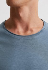 Helles blaues T-Shirt mit Rundhalsausschnitt, aus glattem Stoff gefertigt. Verfügt über eine dezente Textur und eine Naht entlang des Kragens.