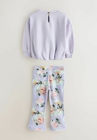 Fialová mikina s zaobleným lemom a zadným zipsom, kombinovaná s legínami s kvetinovým vzorom v odtieňoch fialovej a ružovej, s rozšírenými nohavicami.