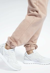 Biele Reebok tenisky majú hladké syntetické a textilné materiály, nízky dizajn, hrubú podrážku a svetlo levanduľové akcenty. Rúžové tepláky s elastickými manžetami.