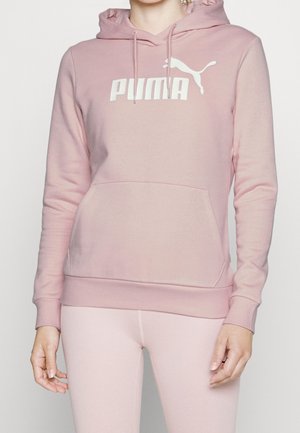 Kvinde iført en lyserød Puma hættetrøje med frontlomme og logo, kombineret med matchende lyserøde leggings.