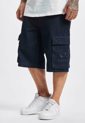 Shorts cargo bleu marine en denim avec deux poches latérales et logo brodé, associés à des baskets blanches. Design décontracté, longueur genou.