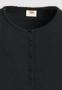 Melns ribspūšs adīts tops ar apaļu kakla izgriezumu, pieci melni pogas priekšpusē un balts Levi's birka iekšpusē apkaklē.