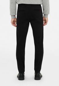 Pantalones negros ajustados, con dos bolsillos traseros y detalles sutiles, combinados con calzado negro y un suéter gris texturizado.