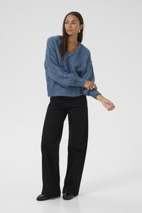 Túlméretezett, kék kötött pulóver bordás ujjakra és szegélyre, fekete, széles lábú nadrággal és lapos fekete cipőkkel párosítva. Egyszerű, melírozott mintázat.