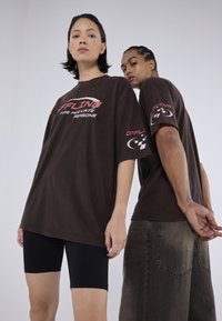 Brune oversized t-shirts med grafisk tekst "OFFLINE FOR PRIVATE REASONS" i pink, parret med sorte cykelsorts og slidte jeans.