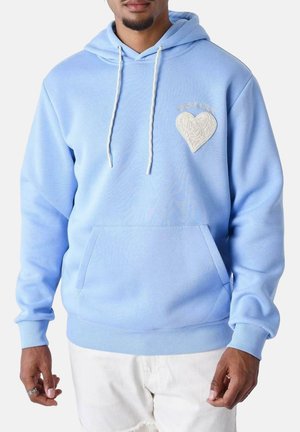 Sweat-shirt bleu clair en tissu doux avec une poche kangourou à l'avant, présentant un patch en forme de cœur texturé sur la poitrine et une capuche avec cordon.