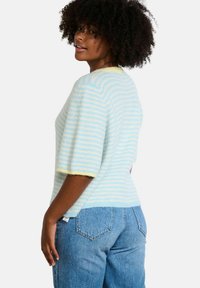 Short-sleeved sweater in light blue and yellow stripes, featuring a soft texture and relaxed fit. Paired with high-waisted denim jeans.
