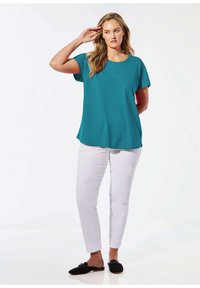 Türkises T-Shirt mit kurzer Arm, Rundhalsausschnitt, kombiniert mit weißen Slim-Fit-Hosen und schwarzen Slip-Ons. Weicher Stoff, lässiges Design.