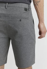 Shorts gris en tissu texturé, dotés d'une poche arrière avec fermeture à bouton et d'une étiquette sur la taille. Design et coupe classiques.