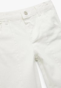 Pantalones de mezclilla blanca con una textura suave, que cuentan con un cierre frontal de botón, bolsillos laterales y detalles cosidos a lo largo de las costuras.