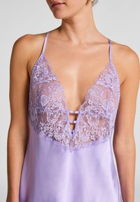 Lavendelkleurige satijnen chemise met kantafwerking, diepe dekollété en dunne bandjes; heeft een keyhole-ontwerp met drie stoflussen in het midden.