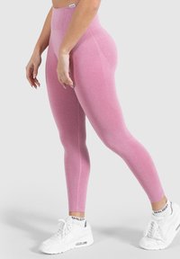 Rosa, hochgeschnittene Leggings mit strukturiertem Design und glatter Stoffqualität, kombiniert mit weißen Sportschuhen mit einem dekorativen Knöcheldetail.